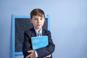 Cheerful European  schoolboy with book in uniform in a classroom. First time to school. Back to school.