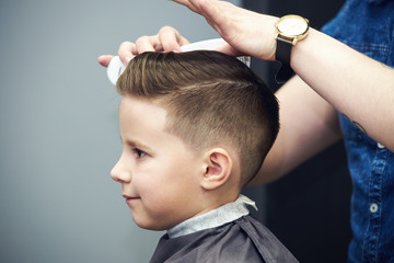 Barber shop. Hairdresser makes hairstyle to a boy using styling gel. - 207538546