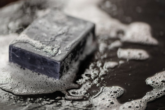 Block Of Natural Carbon Charcoal Soap On Black Stone Background With Bubbles