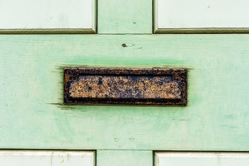 Vintage metal mail slot in door with painted green wood