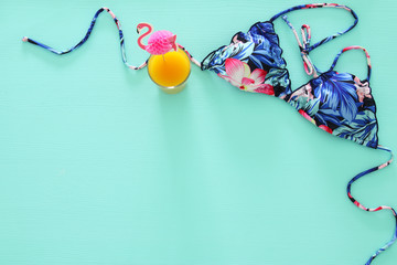 Top view of fashion female swimsuit bikini, fruit coctail on mint wooden background. Summer beach vacation concept.
