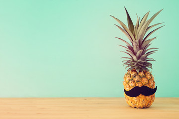 Pineapple on wooden table with funny moustache. Beach and tropical theme.