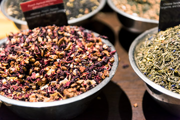 Closeup of apricot herbal tea spices on display in metal bowl tray filled with fruit and berry mix, sign, green herbs