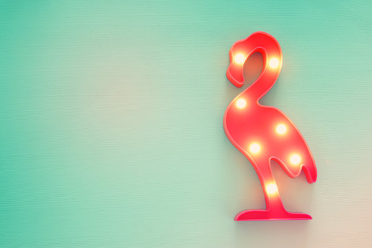 a plastic flamingo lamp with leds over mint wooden background. holiday summer concept.
