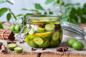 A glass jar filled with unripe walnuts, lemon and spices
