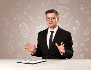 Young handsome businessman sitting at a desk with white mixed media icons behind him