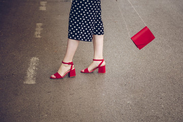 stylish woman in polka dot culottes and red high heel shoes holding a red purse and crossing the road.  street style fashion