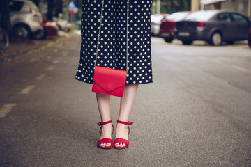 stylish woman in polka dot culottes and red high heel shoes holding a red purse and crossing the road.  street style fashion © mlasaimages