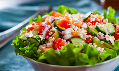 vitamin salad with tomato, cucumber, onion, lettucce and cottage cheese in white bowl on table