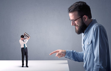 Young professional businessman being angry with an other miniature businessman in front of a blueish grey background