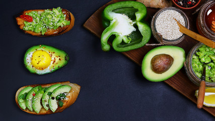 Healthy lunch snack, three delicious avocado sandwiches, fresh sliced avocados, pepper, lemon, sesame seeds copy space on a black stone background, copy space, top view, set