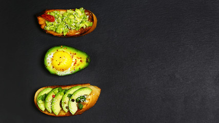 Healthy lunch snack, three delicious avocado sandwiches, fresh sliced avocados copy space on a black stone background, copy space, top view, set
