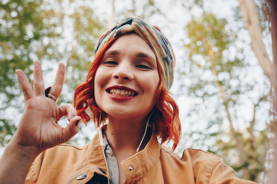 beautiful and stylish red haired girl taking a selfie with her smartphone outdoors
