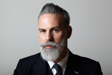 Portrait of elegant middle aged bearded gentleman wearing trendy suit over empty gray background....
