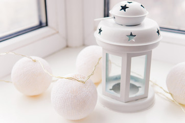 Fototapeta na wymiar White candleholder and cotton light ball garland on the window sill.