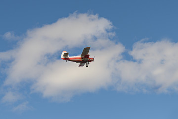 old orange biplane flying in a blue sky with clouds