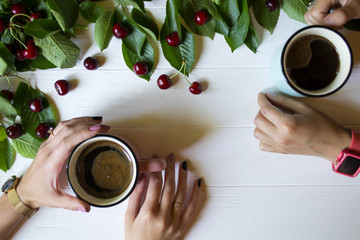 Female hands with coffee against a white wooden background, with ripe cherries. Top view.