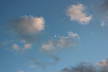 Fototapeta na wymiar a thin crescent in the early evening is visible in the sky among the white clouds