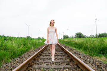 Eine junge hübsche Frau läuft auf stillgelegten Bahngleisen, im Hintergrund Windräder