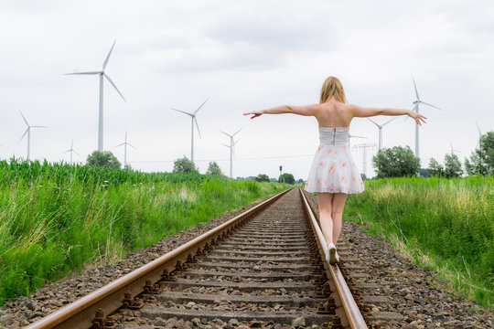 Eine junge h&uuml;bsche Frau l&auml;uft auf stillgelegten Bahngleisen, im Hintergrund Windr&auml;der