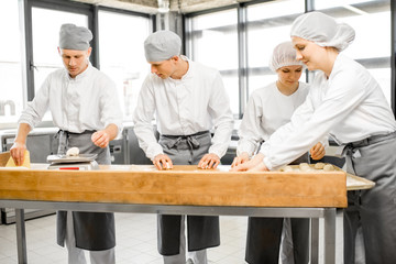 Group of young workers in uniform forming dough for baking on the wooden table standing together at the modern manufacturing