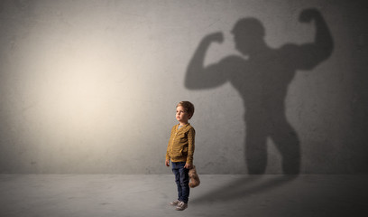 Little waggish boy in an empty room with musclemen shadow behind
