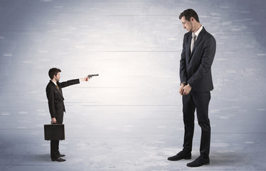 Tiny businessman with gun shooting giant fearful businessman
