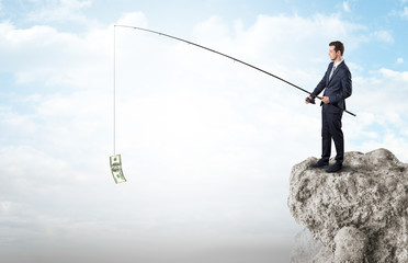 Elegant young businessman fishing cash from a huge rock