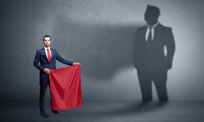 Businessman standing with red cloth on his hand and his shadow on the background
