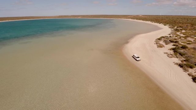 An aerial shot of a coast and sea with a ute driving on lands