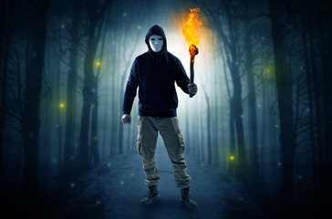 Mysterious man coming from a path in the forest with burning flambeau concept
