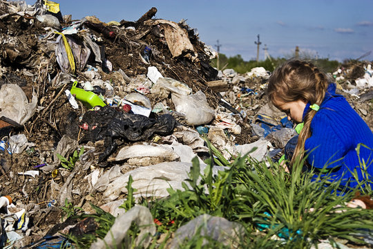A small beggar girl in a garbage dump scatters rags