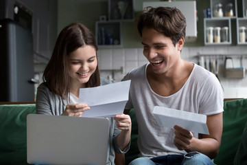 Happy young couple excited by reading good news in paper letter about refund tax money, millennial...