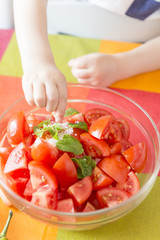 Hands of a child putting salt in a bowl with vegetables