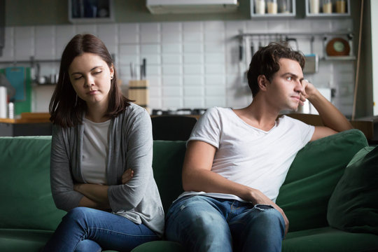 Unhappy millennials ignoring avoiding not talking after fight, frustrated couple in quarrel sitting silent on couch at home having disagreement thinking of misunderstandings in bad relationships