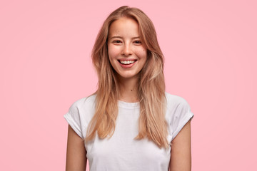 Positive young female with pleasant smile, has healthy skin, wears casual white t shirt, spends...