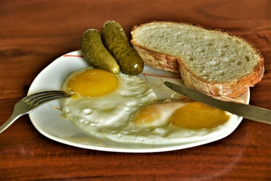 fried eggs on a plate with pickled cucumbers and a slice of bread