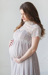 A pregnant woman with long hair and in a beautiful long dress. Pregnant hugs belly