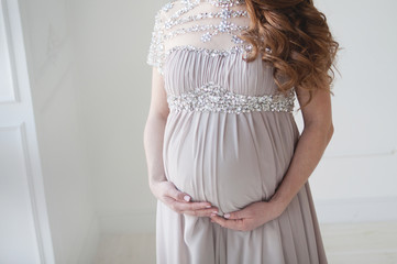 A pregnant woman with long hair and in a beautiful long dress. Pregnant hugs belly