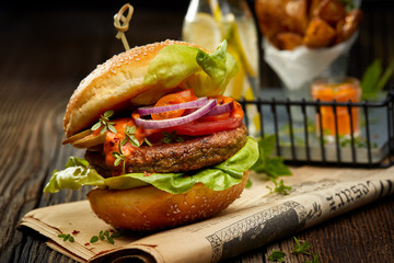 Falafel burger with addition of lettuce, tomato, onion, pickle cucumbers, spicy aromatic sauce and herbs on a wooden rustic table. Vegetarian food tasty and nutritious