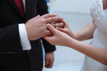 A woman puts a gold ring on the finger of a beloved man. Wedding day of loving people. French manicure at the bride.