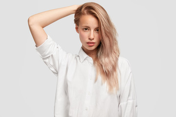 Isolated shot of nice pretty female with long hair combed on one side, looks pleasantly and calmly, wears loose man`s shirt, isolated over white background. People, beauty and leisure concept