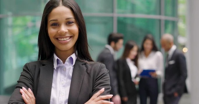 Portrait of a business woman, in a suit and tie, happy and smiling as she looks at the camera and in the background a group of multi-ethnic business people. Concept of: success and female career