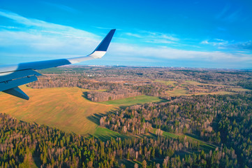 Airplane window view. View from the window on the spring forest, meadows, blue sky. Airplane's wing flying above the colorful land