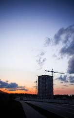 Crane and construction site against sunset. Unfinished building construction and building cranes against blue sky background. Concept of urban development