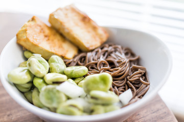 Soba buckwheat noodles Japanese food macro closeup, fried baked golden crispy tofu, green fava beans on hot, cold summer, white bowl