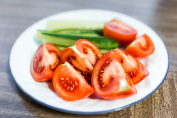 Macro closeup of fresh sliced juicy ripe tomatoes and cucumbers slices on plate, wooden table as healthy snack or salad appetizer