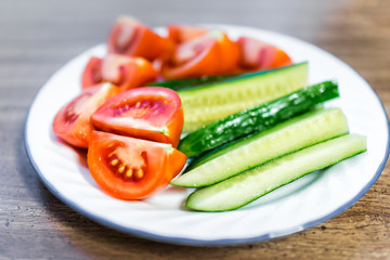 Fresh sliced juicy ripe tomatoes and cucumbers slices on plate macro closeup, wooden table as healthy snack or salad appetizer