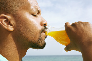 Healthy organic food. Portrait of dark skinned guy drinking tasty fresh orange juice. African man...