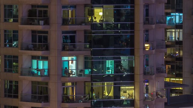 Windows of the multi-storey building of glass and steel lighting inside and moving people within timelapse
